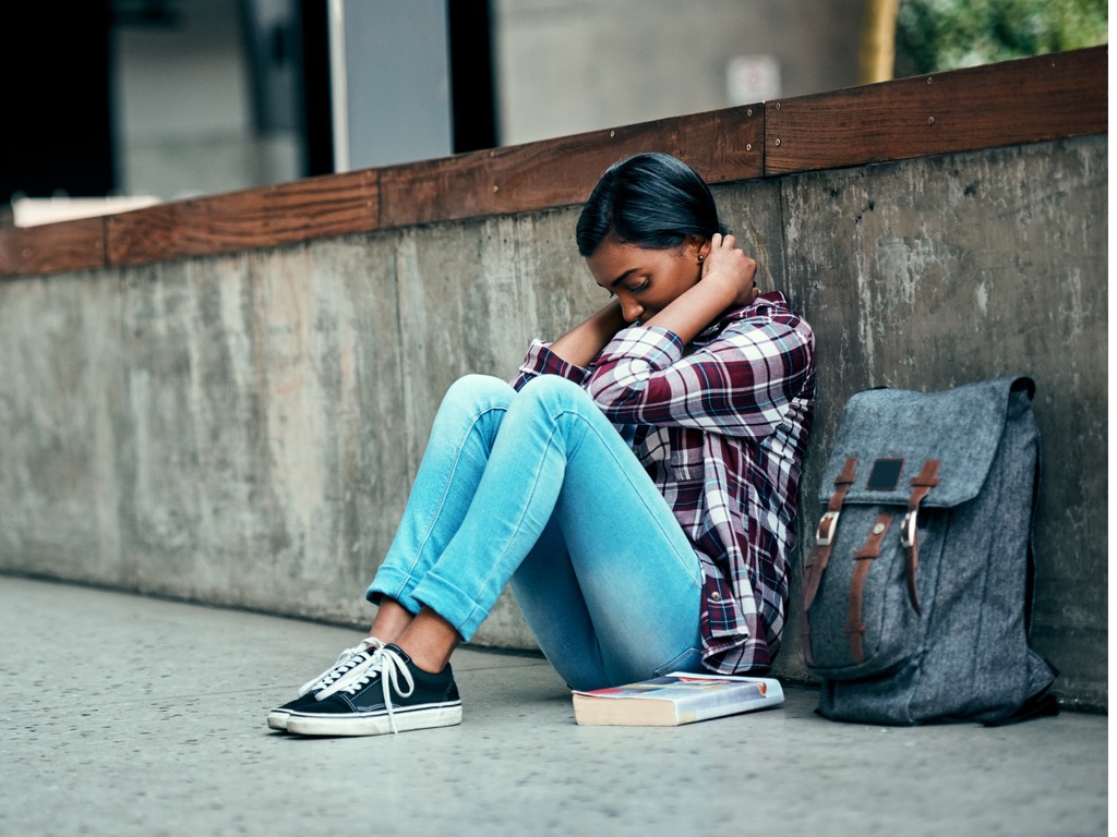 female-college-student-sitting-on-ground-with-knees-pulled-towards-chest-and-hands-near-head-while-dealing-with-symptoms-of-substance-abuse