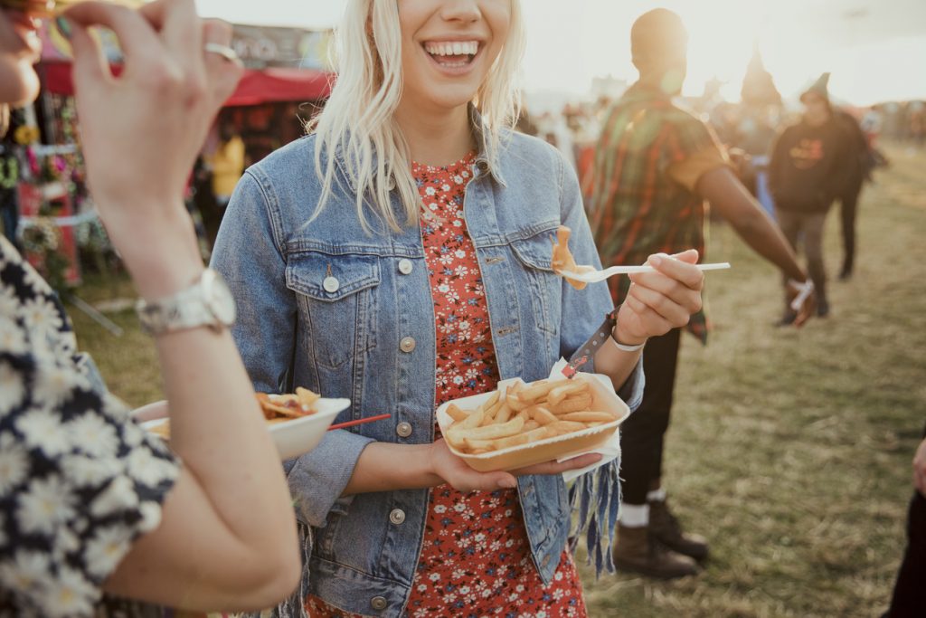 young-woman-smiling-while-eating-food-at-outdoor-festival-with-her-friends